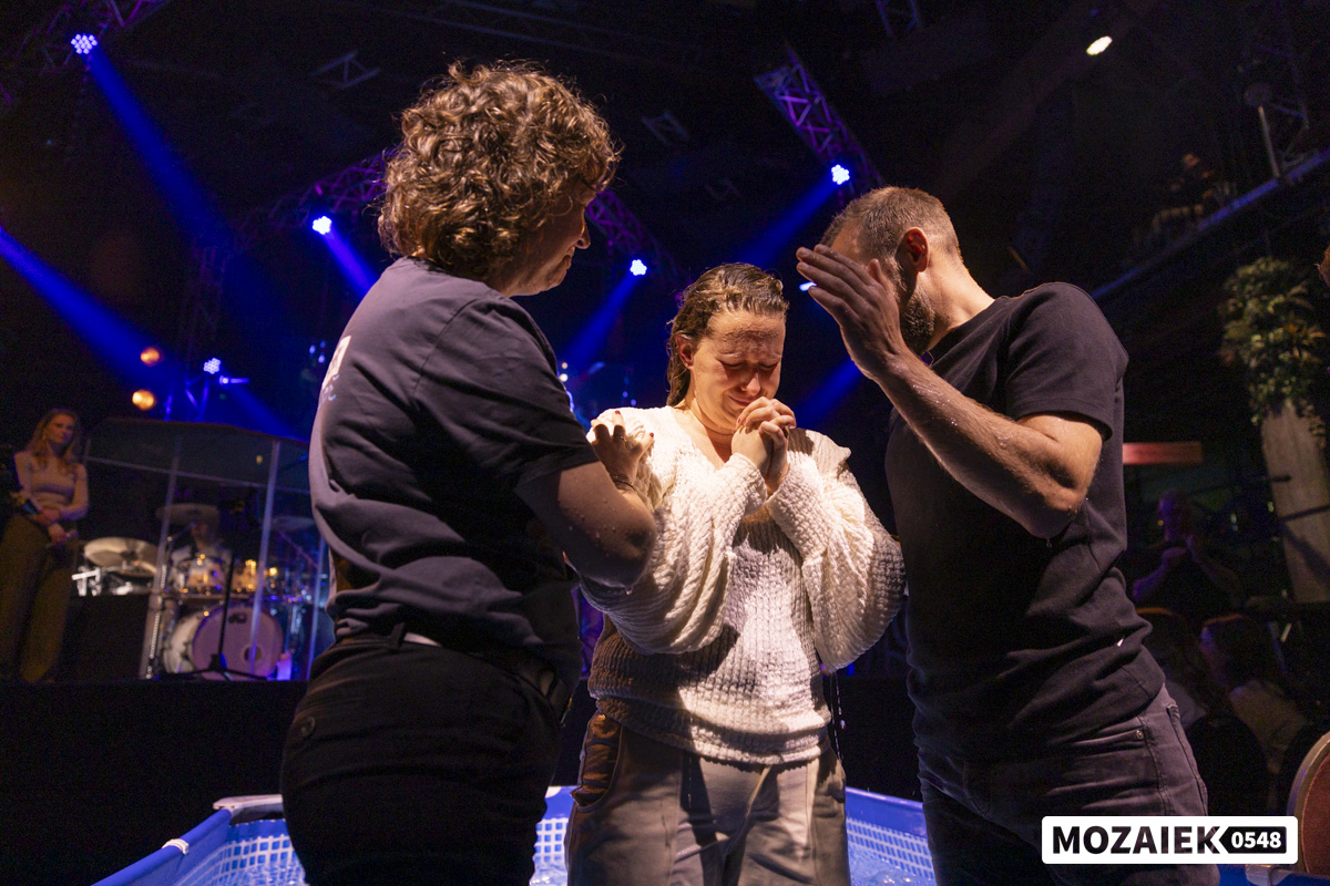 Twee voorgangers leggen de handen op en bidden voor een vrouw tijdens de doopdienst van Mozaiek0548