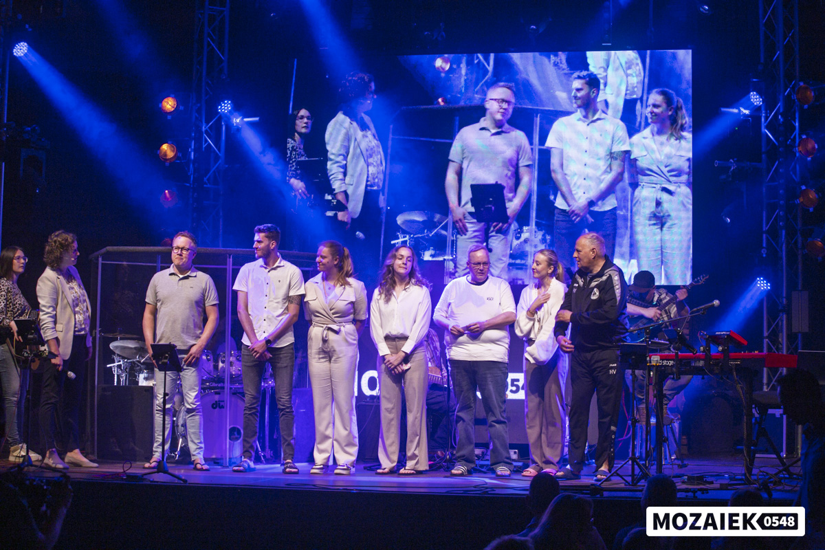Groep dopelingen en voorgangers staat samen op het podium tijdens de doopdienst van Mozaiek0548