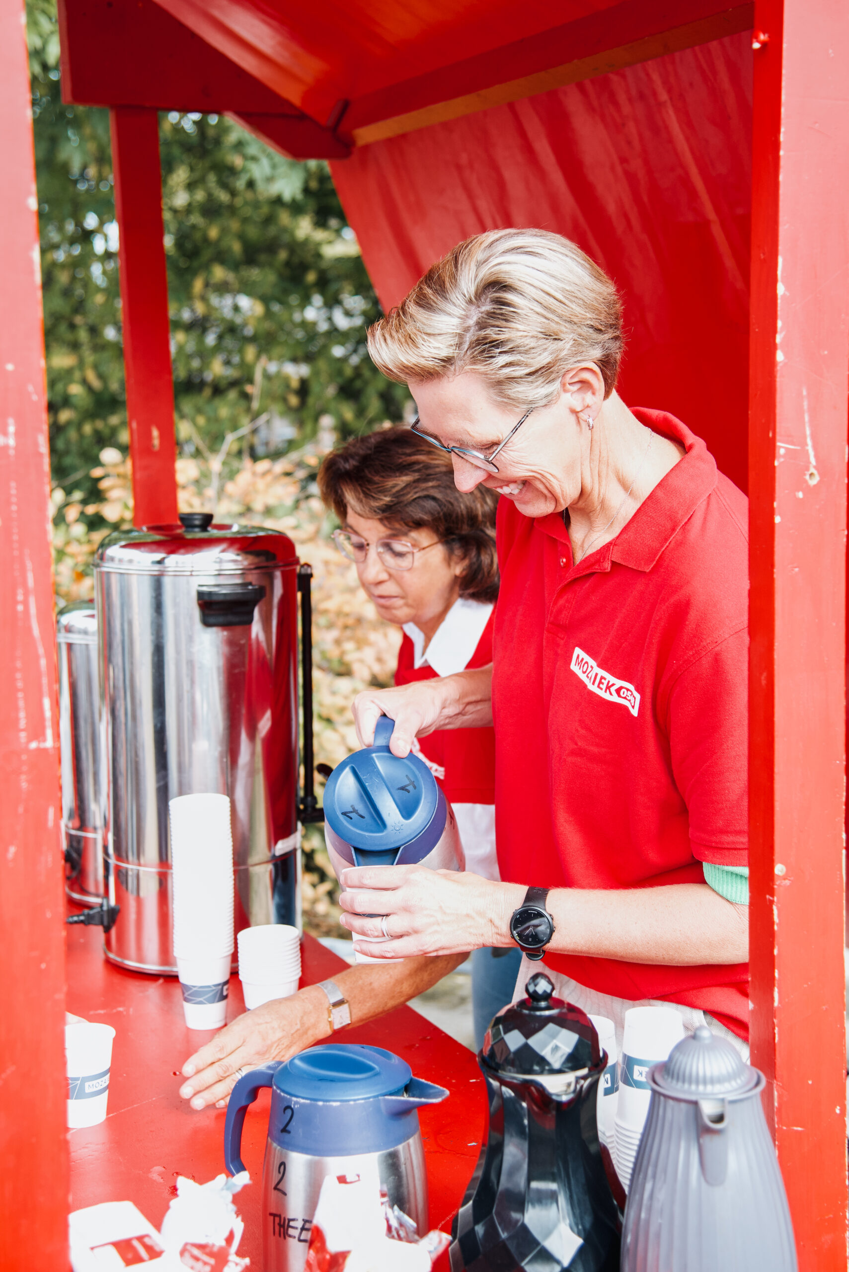 Vrijwilligers schenken koffie en limonade bij een kraam tijdens de buitendienst