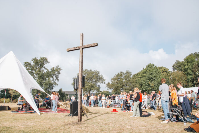 Groot houten kruis in het veld met een witte tent en bezoekers tijdens de buitendienst