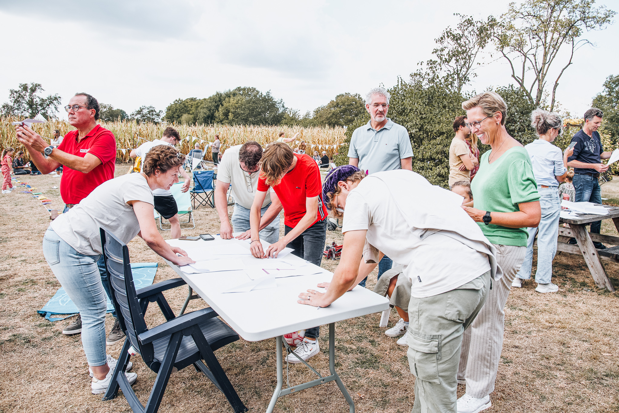 Bezoekers vouwen papieren vliegtuigjes rond een tafel op het veld