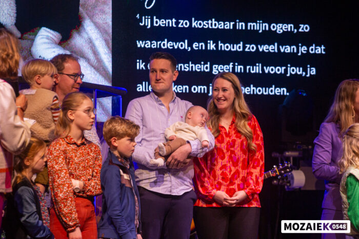 Gezinnen staan op het podium terwijl er een bijbeltekst op het scherm wordt geprojecteerd