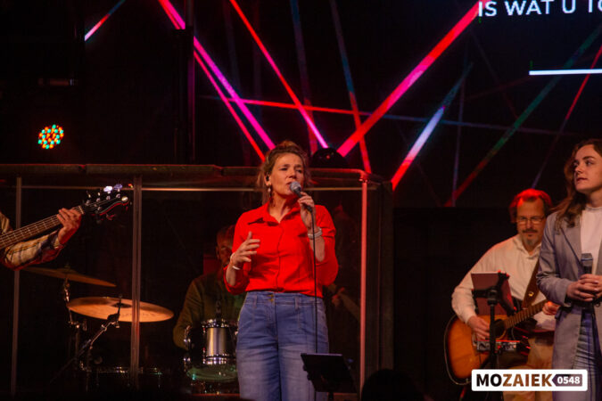 Een zangeres zingt in de microfoon terwijl de band achter haar speelt tijdens een dienst van Mozaiek0548