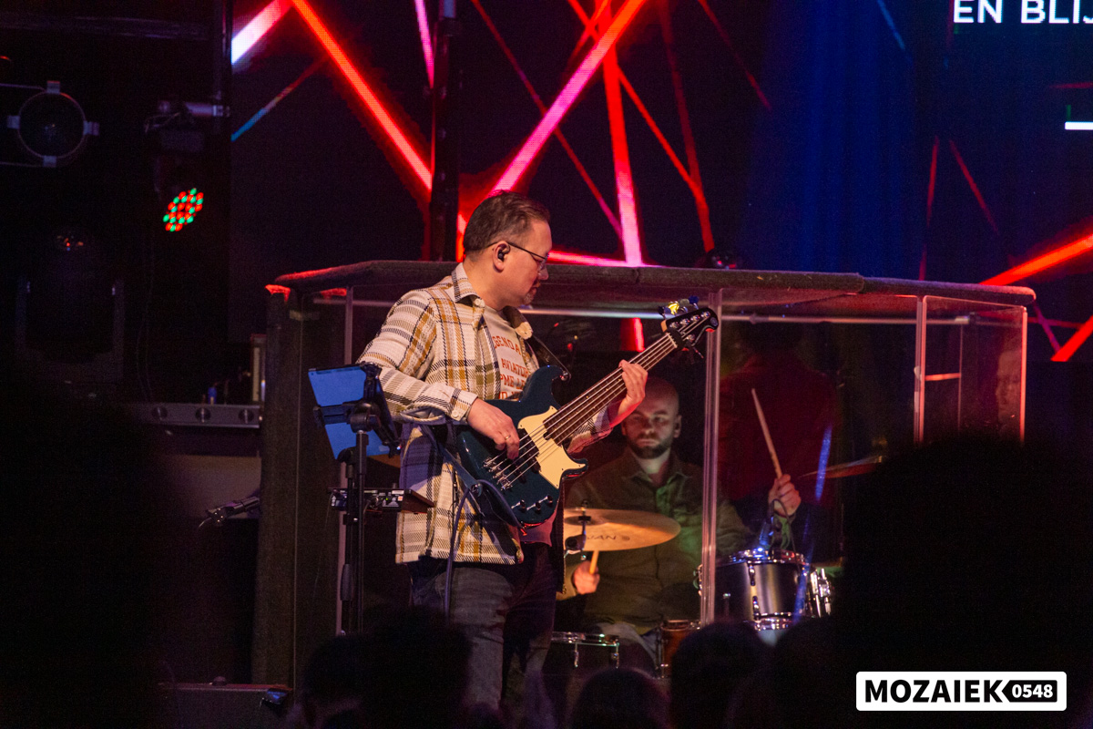 De bassist speelt op het podium met de drummer achter zich tijdens een dienst van Mozaiek0548
