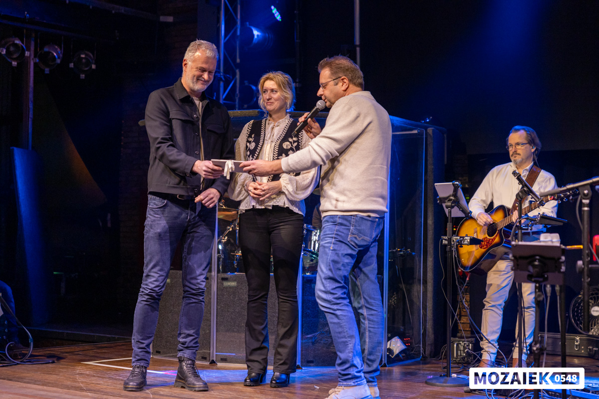 Drie mensen staan samen op het podium in gesprek tijdens een dienst van Mozaiek0548