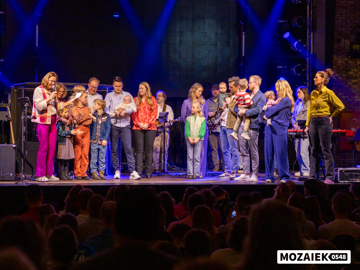 Gezinnen staan op het podium terwijl de volle zaal meekijkt tijdens een opdraagdienst van Mozaiek0548