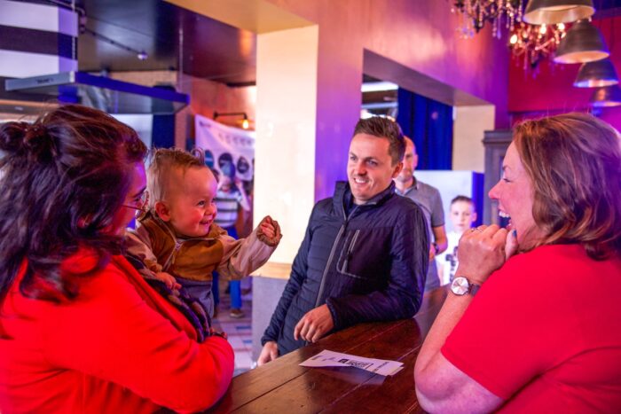 Gastvrouw in gesprek met bezoekers en een kind bij de welkomstbalie