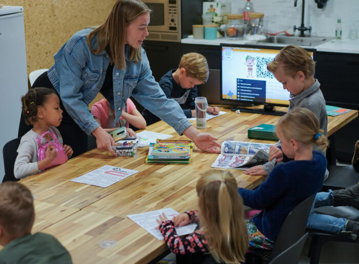 Een vrijwilliger helpt kinderen aan tafel met boekjes en knutselwerk bij Mozaiek Kids