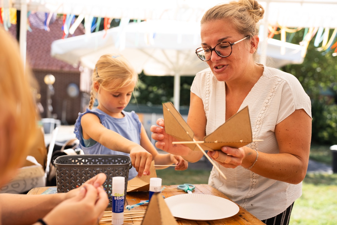 Begeleidster geeft kinderen uitleg bij de knutselopdracht aan tafel tijdens de Kidsdag van Mozaiek0548