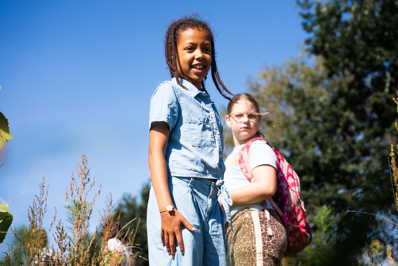 Meisje staat buiten in de zon met andere kinderen op de achtergrond tijdens de Kidsdag van Mozaiek0548