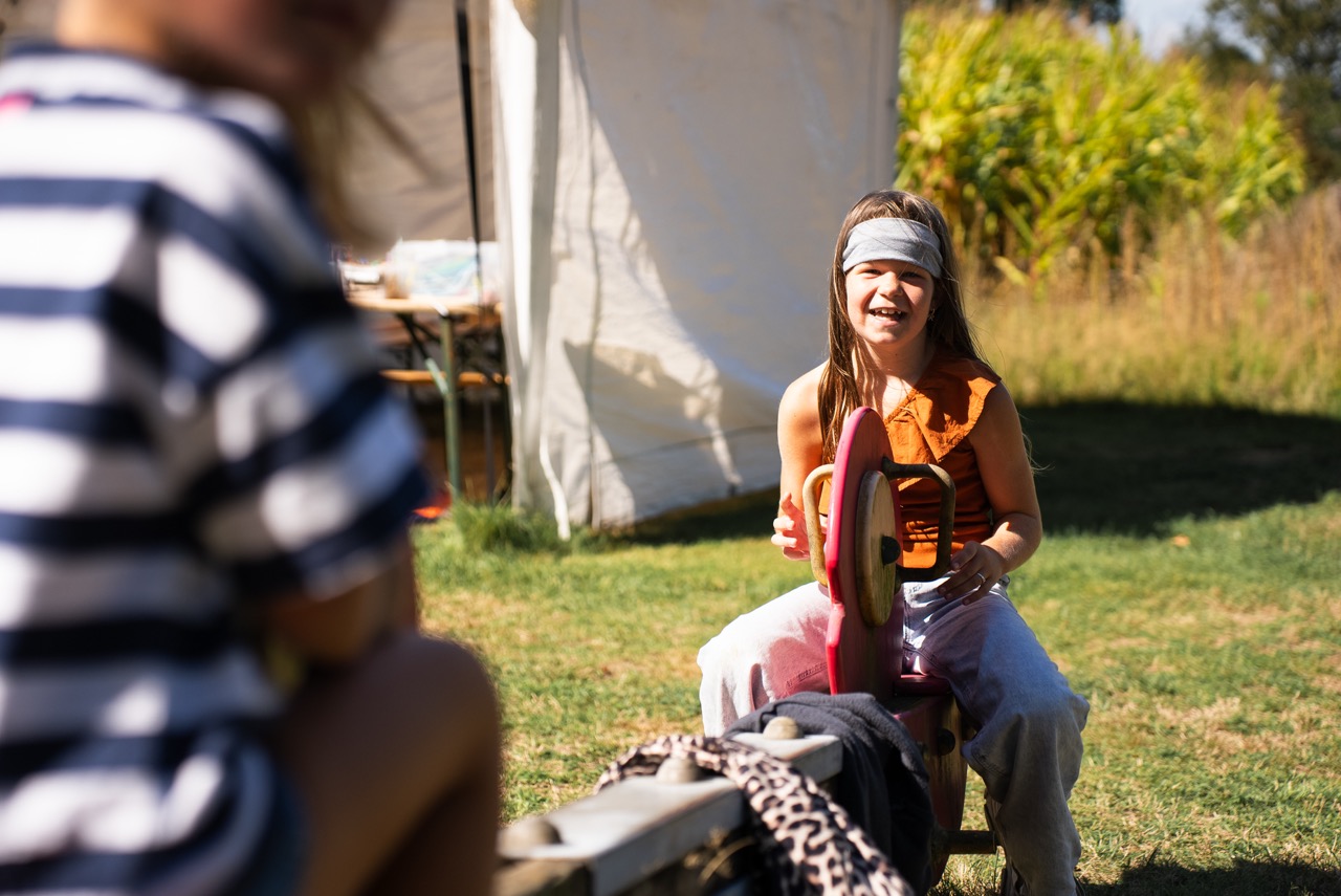 Geschminkt meisje zit op een bankje bij de tent tijdens de Kidsdag van Mozaiek0548