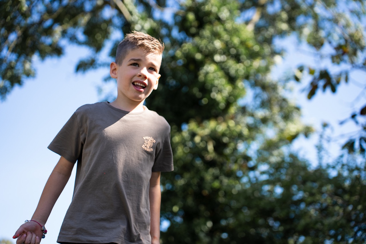 Jongen staat buiten in de zon onder de bomen tijdens de Kidsdag van Mozaiek0548