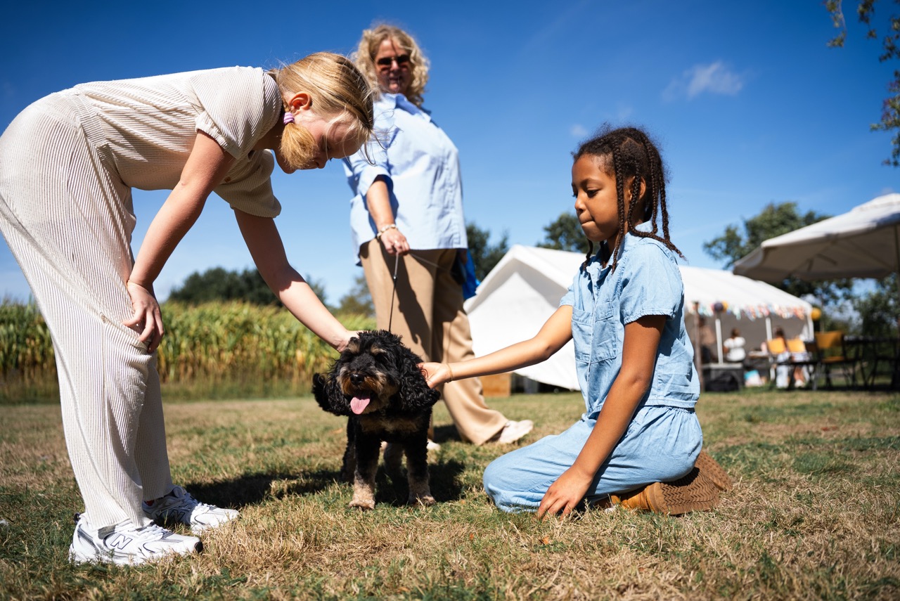 Kinderen en een begeleidster aaien samen een hond in het gras tijdens de Kidsdag van Mozaiek0548