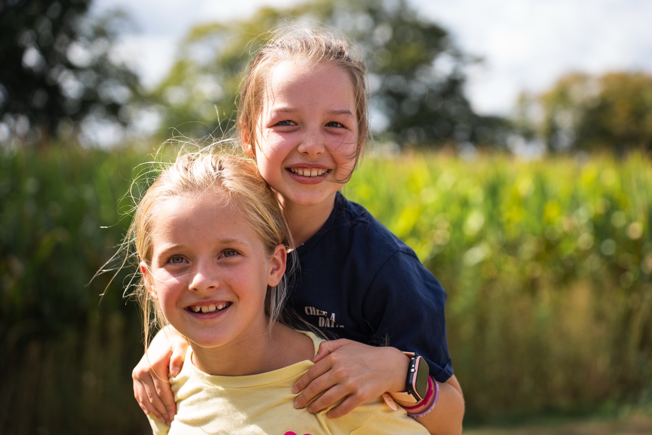 Twee meisjes lachen en knuffelen voor het maisveld tijdens de Kidsdag van Mozaiek0548