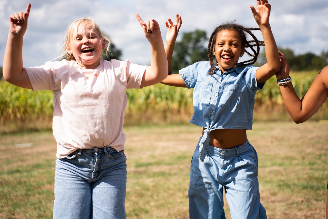Twee meisjes juichen met de armen omhoog in het veld tijdens de Kidsdag van Mozaiek0548