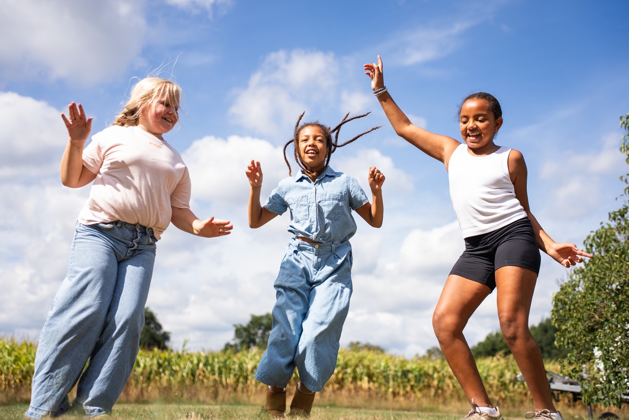 Kinderen springen met de armen omhoog in het veld bij het mais tijdens de Kidsdag van Mozaiek0548