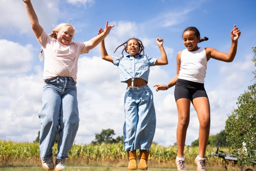 Drie kinderen springen tegelijk omhoog met de armen in de lucht tijdens de Kidsdag van Mozaiek0548
