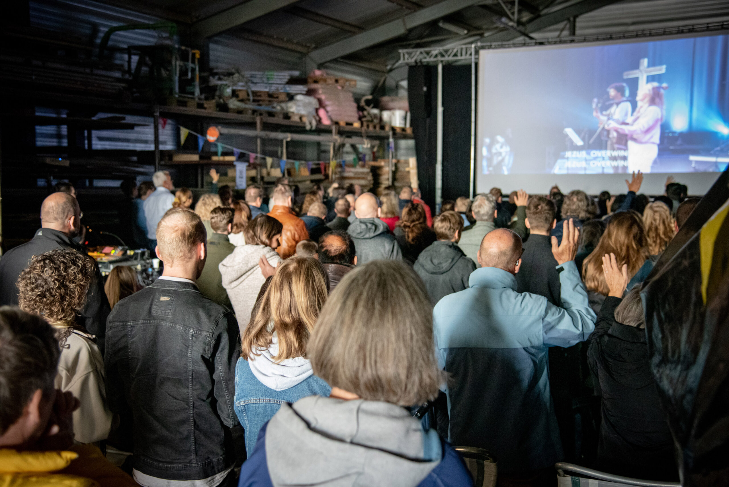 Bezoekers kijken naar de dienst op het grote scherm in de zaal