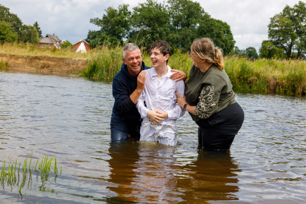 Twee voorgangers dopen een jongen in het open water buiten
