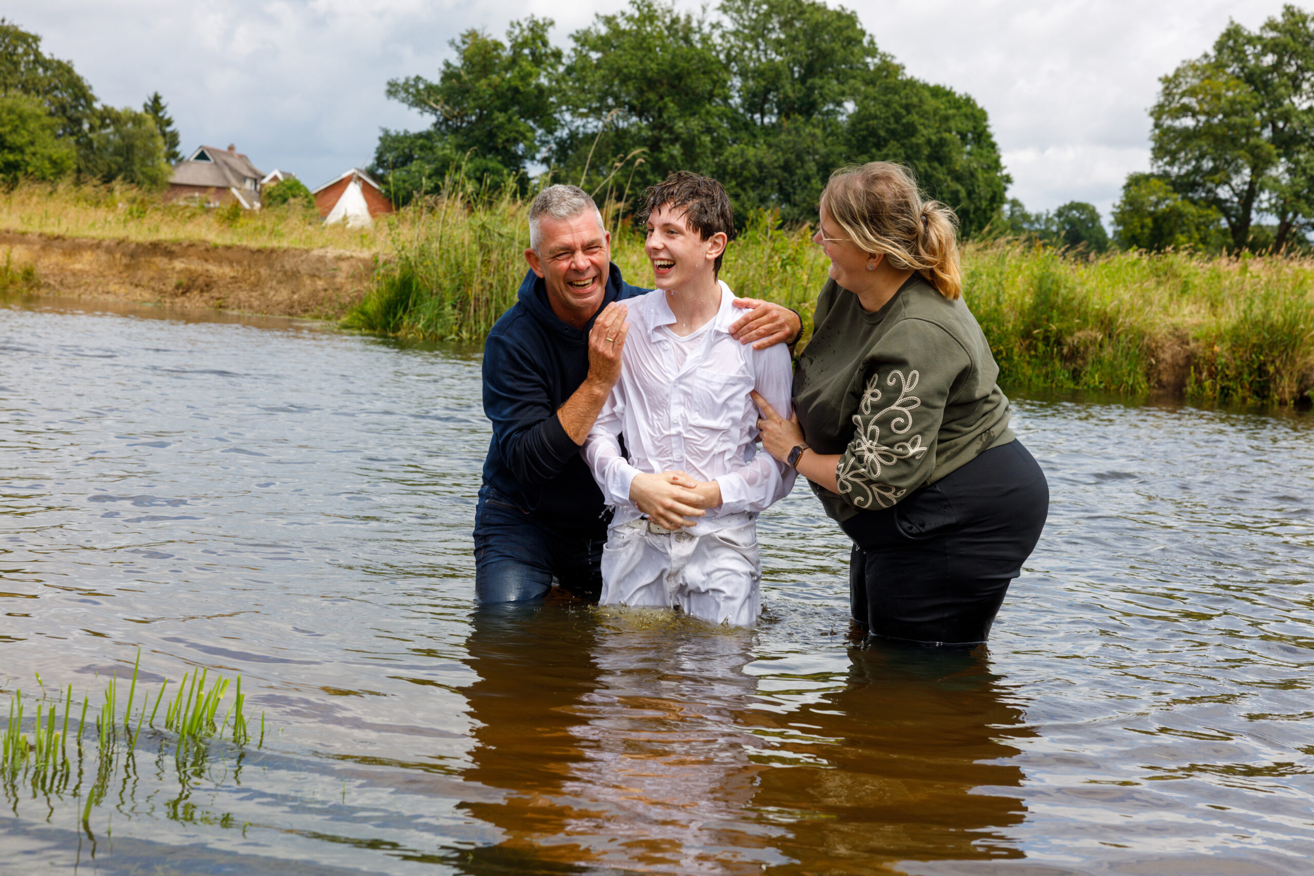 Twee voorgangers dopen een jongen in het open water buiten