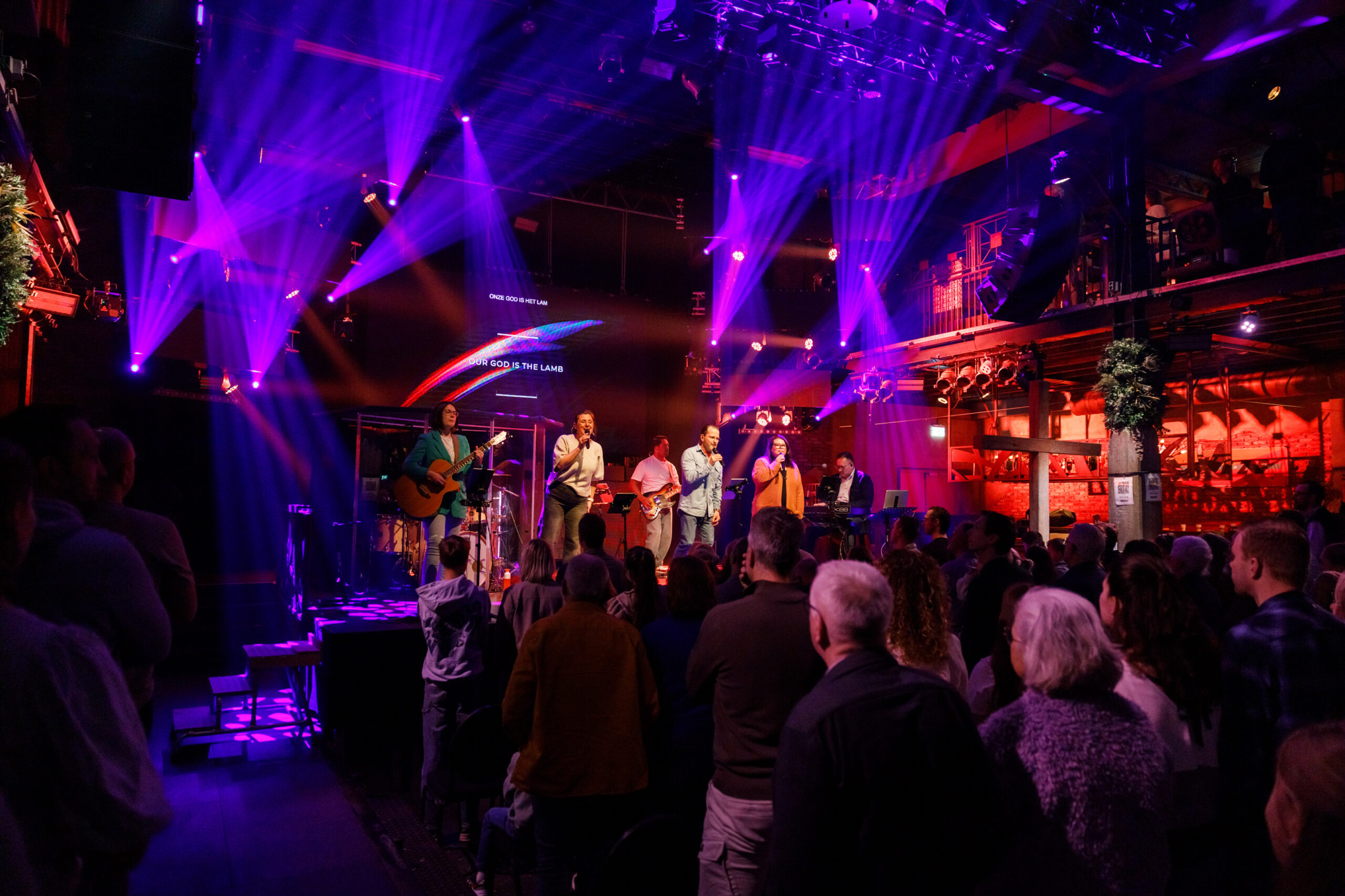 Bezoekers in de zaal met paars en rood licht tijdens de samenkomst
