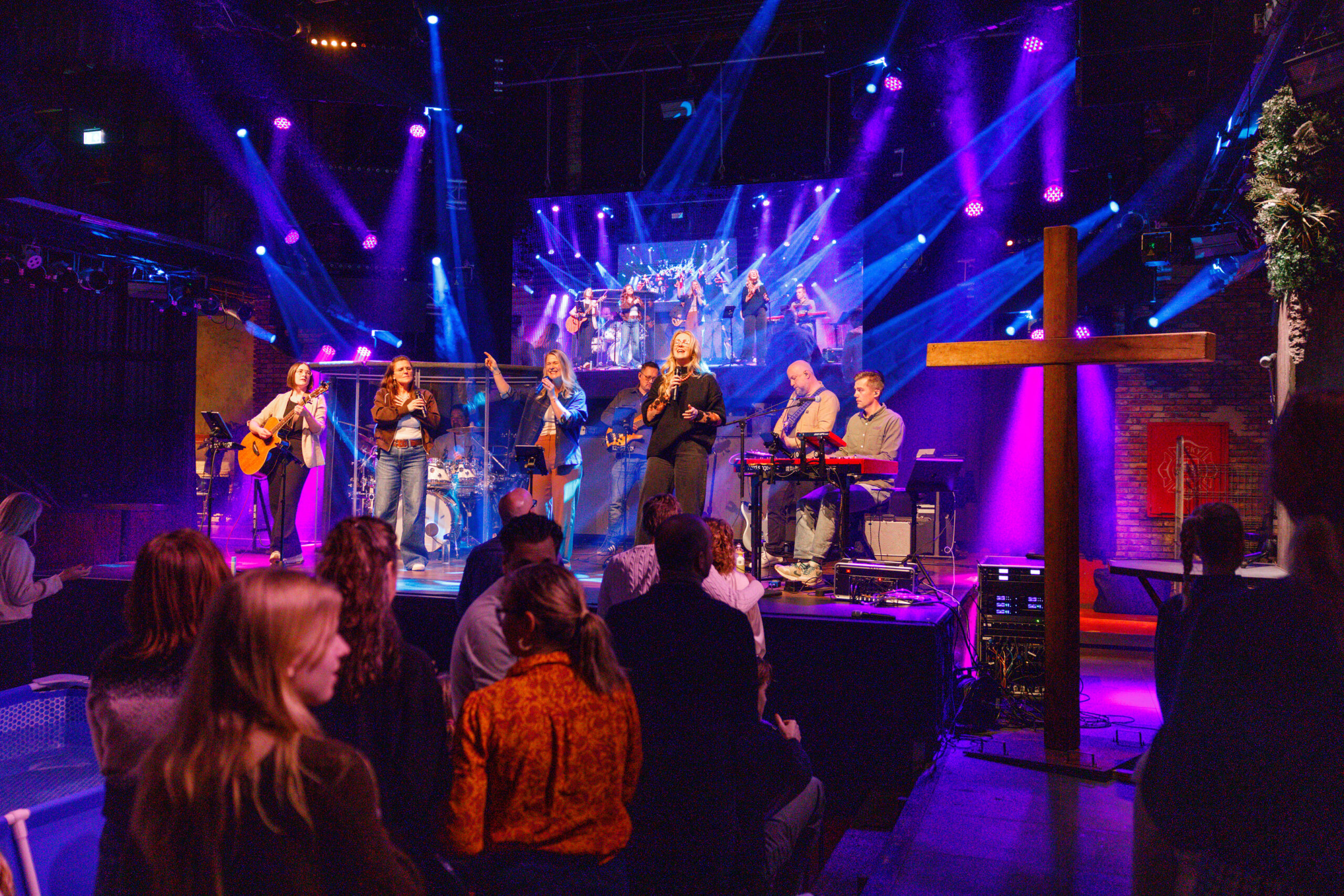 De band speelt op het podium naast het houten kruis, gezien vanuit de zaal