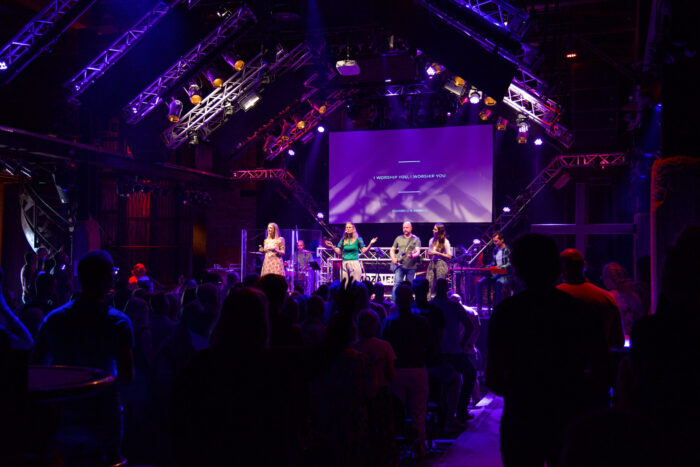 Overzicht van de volle zaal met podium en scherm tijdens de samenkomst