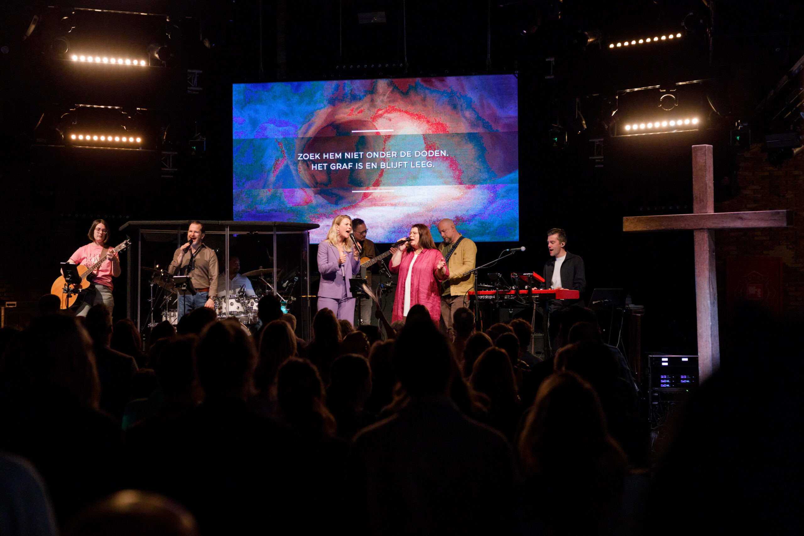 Zangers en band op het podium met de liedtekst op het scherm achter hen