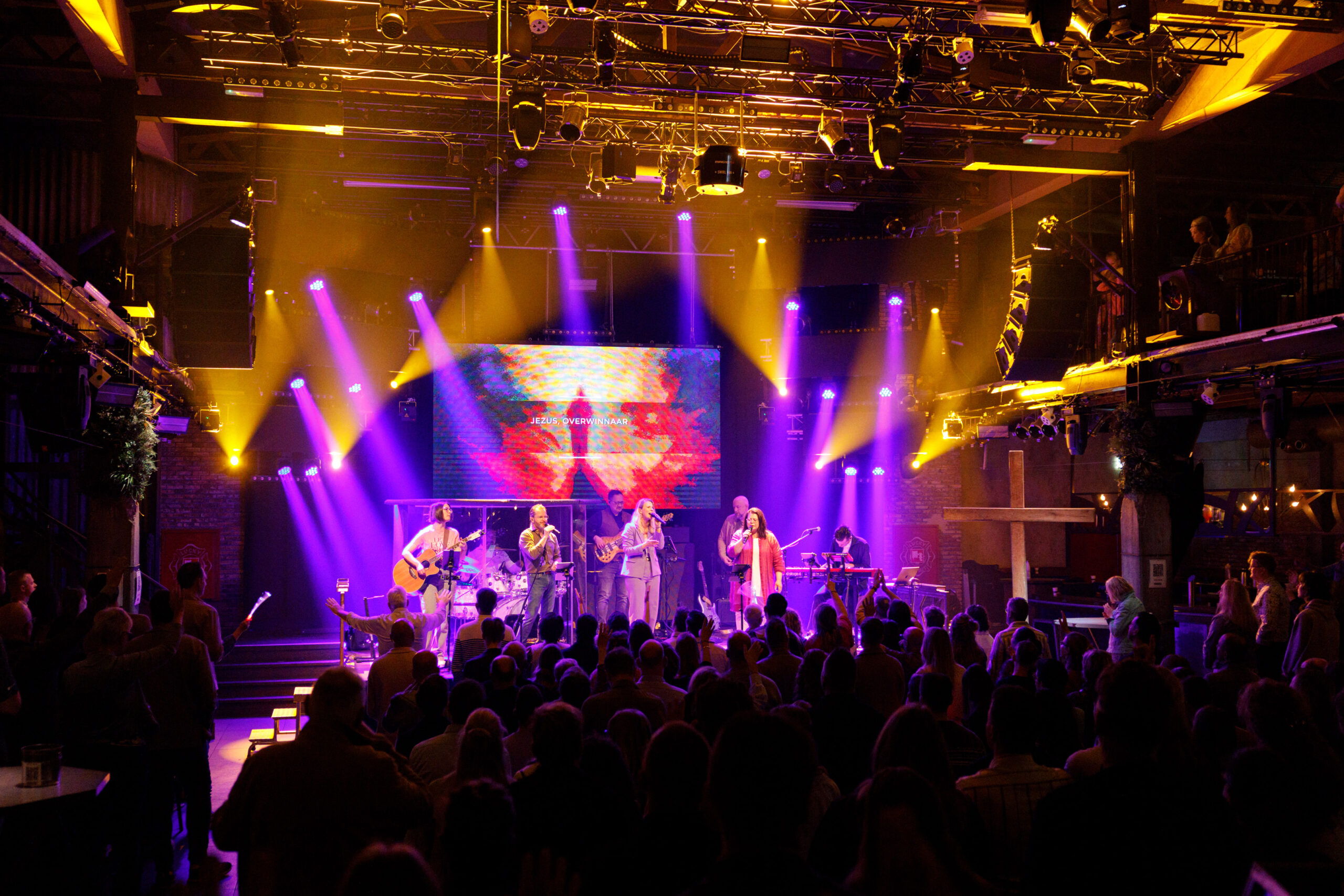 Overzicht van de zaal met bezoekers en de band op het podium in warm licht