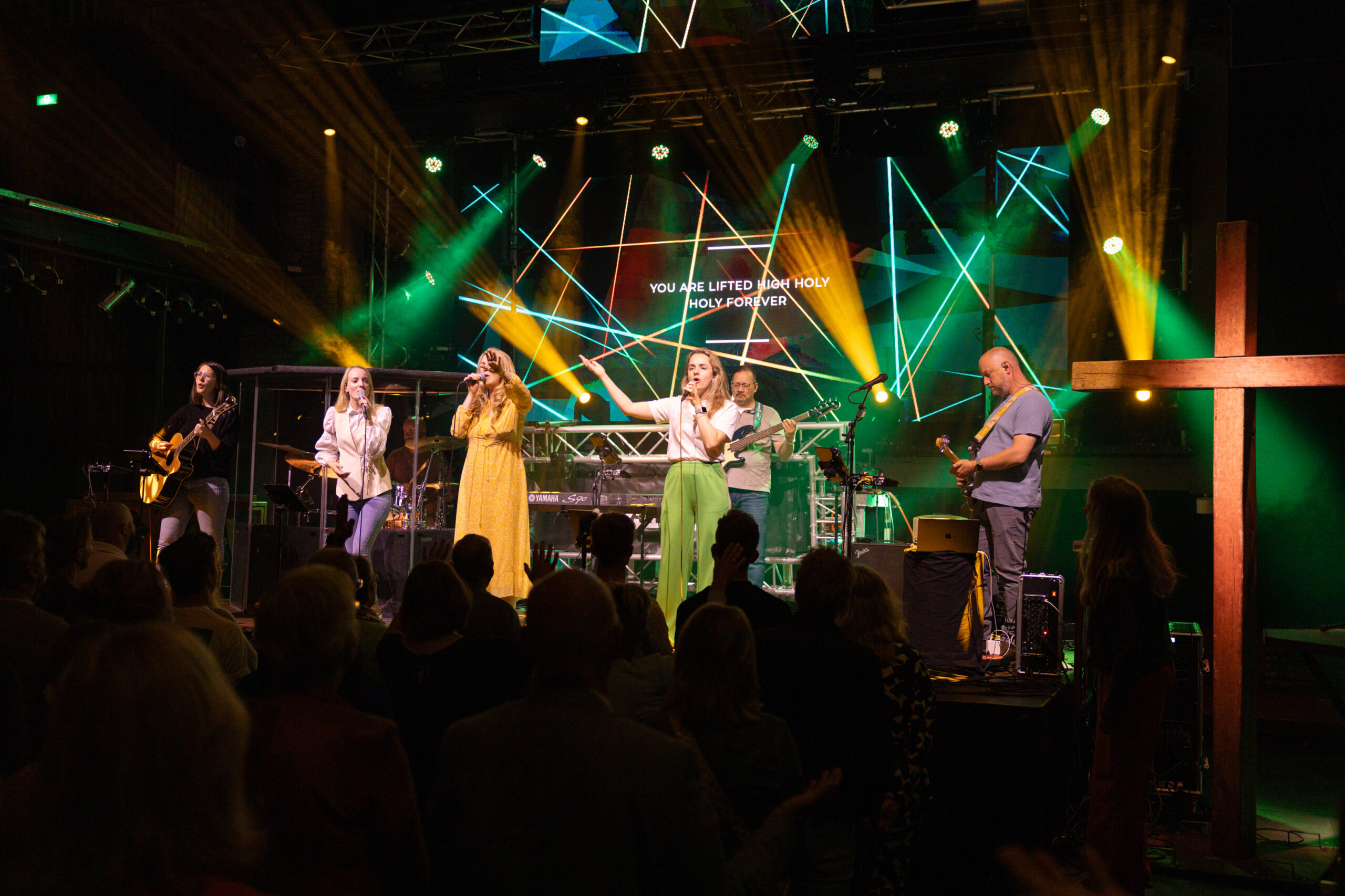 Worshipband met drie zangeressen op het podium van Mozaiek0548 met groene en gele lichtshow