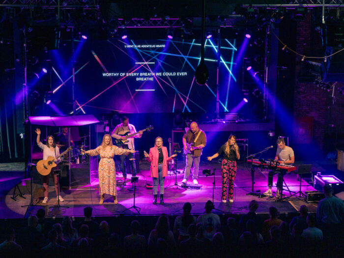 Worshipband van Mozaiek0548 op een roze en paars uitgelicht podium met songtekst op het LED-scherm
